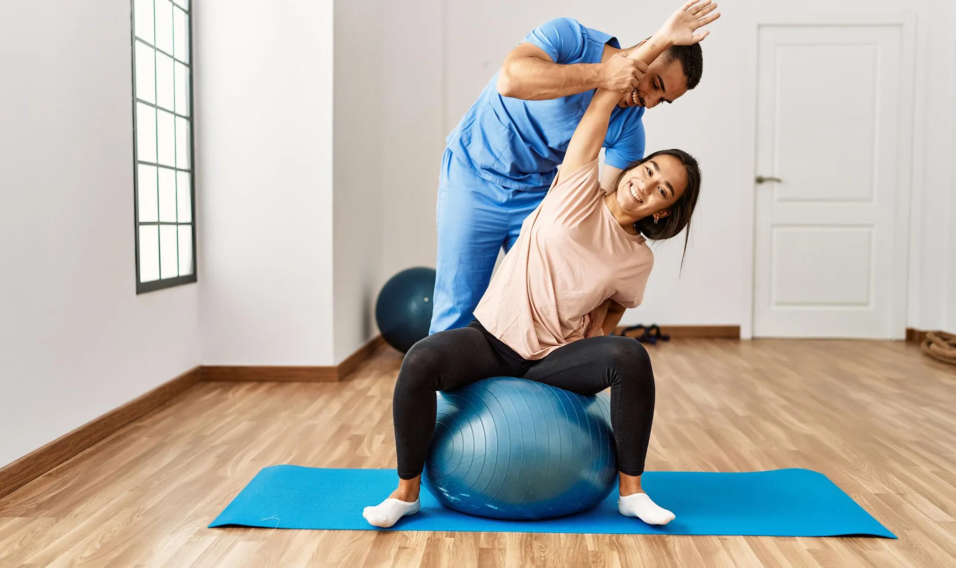 Bewegungstherapie im Reha-Zentrum Gröbming – Physiotherapeut unterstützt Patientin bei Dehnübung auf Gymnastikball